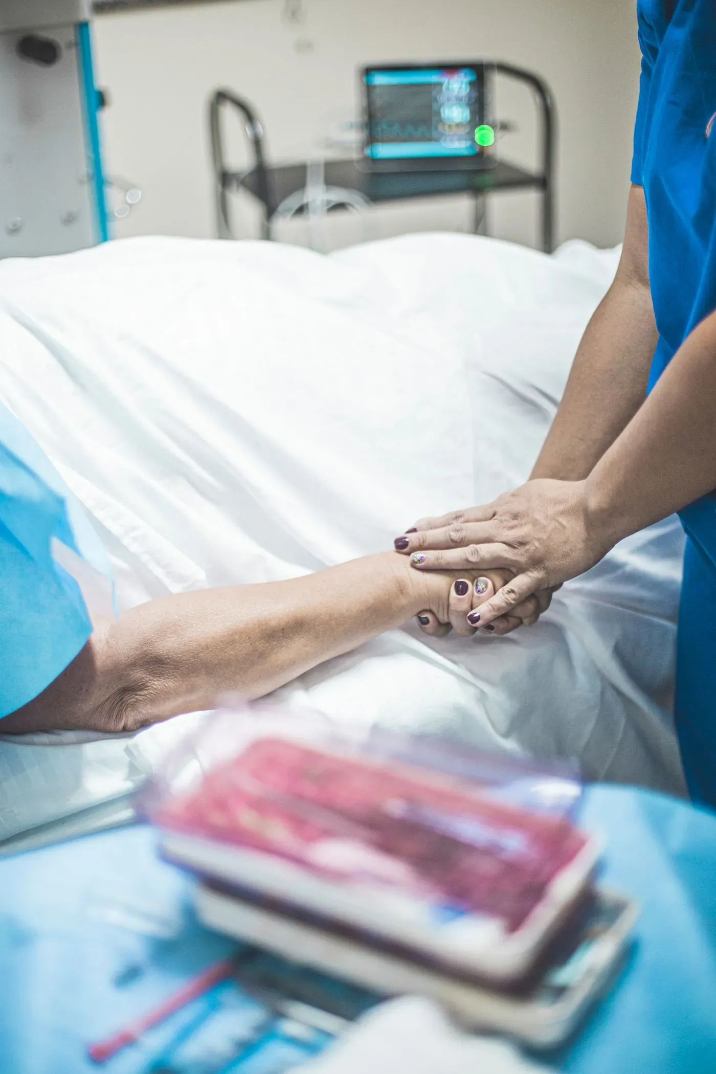 A nurse holding the hand of a patient resting in bed